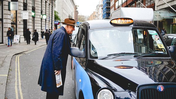 An elderly man speaking to a taxi driver to ask for a lift