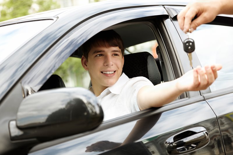 A young driver sitting in a car being passed the keys