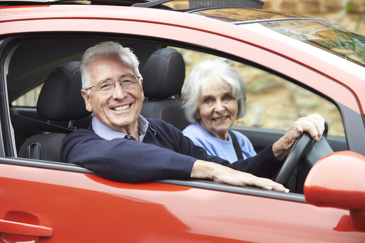 An elderly man and his wife smiling as they drive